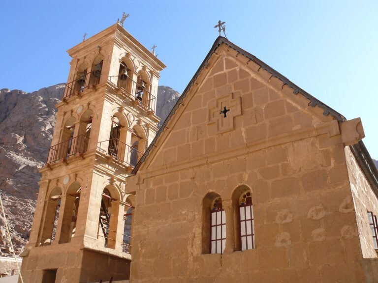Campanario de piedra dorada del Monasterio de Santa Catalina junto a la fachada de la basilica historica con montanas del Sinai detras, Egipto