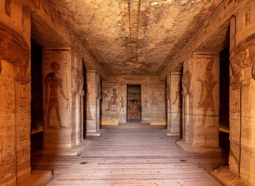 The interior hypostyle hall of the Great Temple at Abu Simbel, Osiride pillars down both sides and painted reliefs leading to the lit sanctuary at the far end