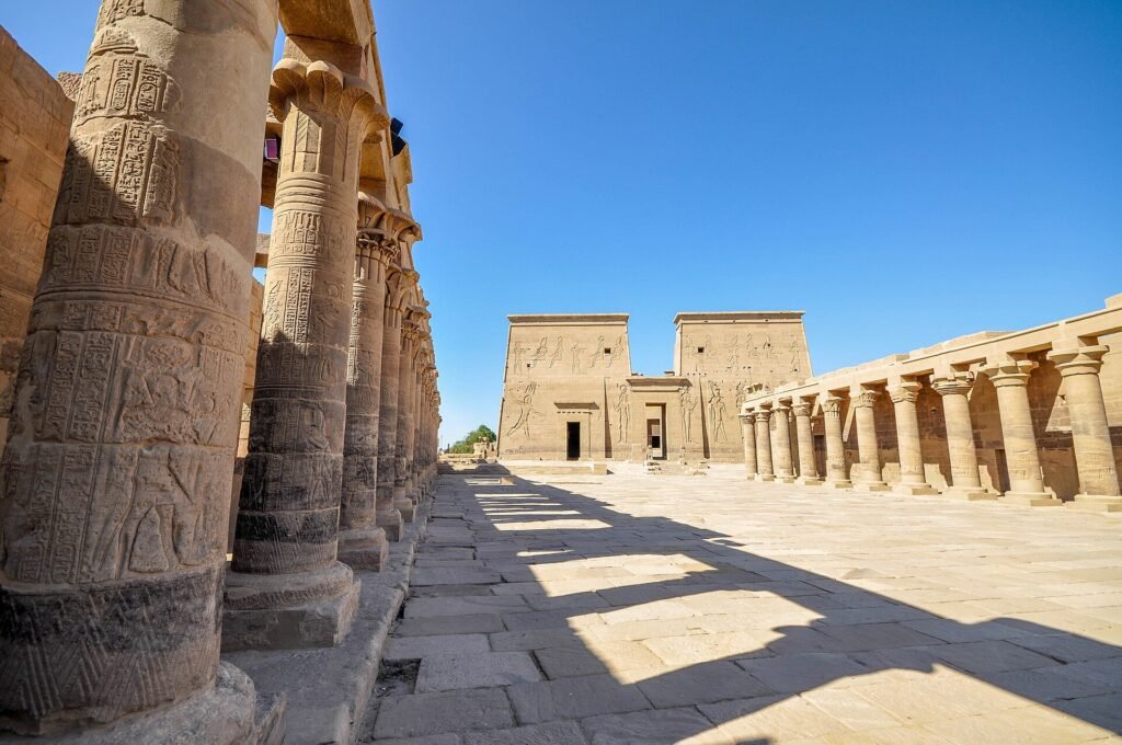 Columnata del Templo de File en Asuan Egipto, con columnas talladas con jeroglificos y el primer pilono al fondo bajo un cielo azul intenso