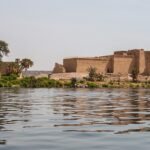 El Templo de File sobre su isla visto desde el agua del Nilo en Asuán Egipto, rodeado de palmeras y acacias con el reflejo en el río