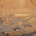 Vista elevada del Templo de Hatshepsut en Deir el-Bahari, sus terrazas escalonadas y columnatas recortadas contra los enormes acantilados dorados de Luxor al atardecer