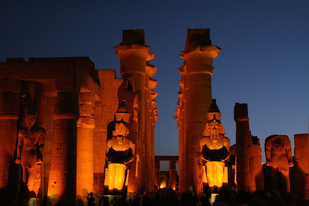 Templo de Luxor iluminado al anochecer con colosos de Ramses II, Egipto, bajo cielo azul crepuscular