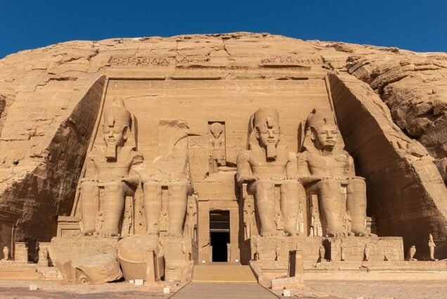 The Great Temple of Ramesses II at Abu Simbel seen head on, the four seated colossi and the sandstone cliff above them against a deep blue sky