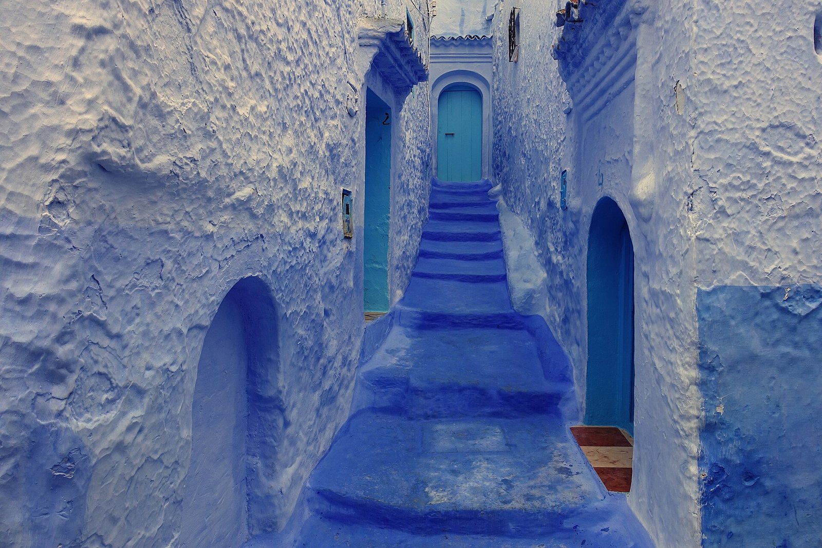 Calleja escalonada pintada de azul intenso en Chefchaouen la ciudad azul de Marruecos con peldanos y puertas azules subiendo entre muros encalados