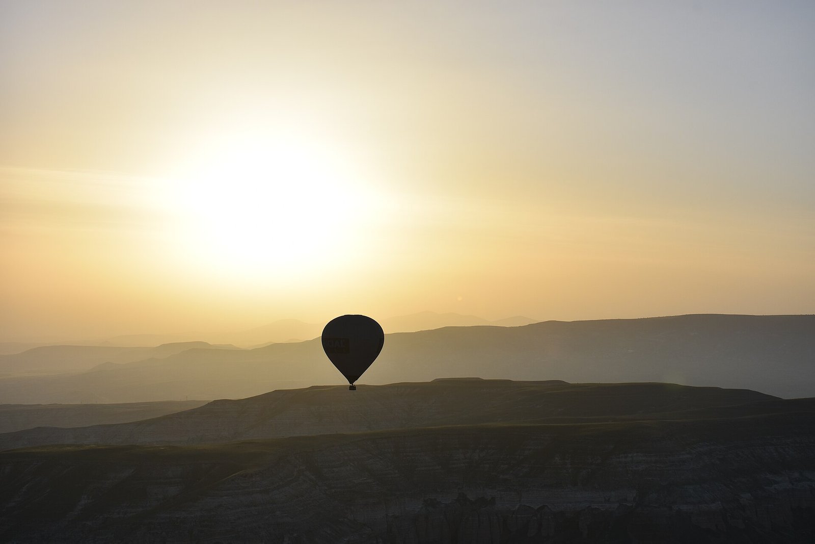 Silueta de un globo aerostatico flotando al amanecer sobre las colinas neblinosas de Capadocia en Turquia, recortado contra el sol naciente dorado