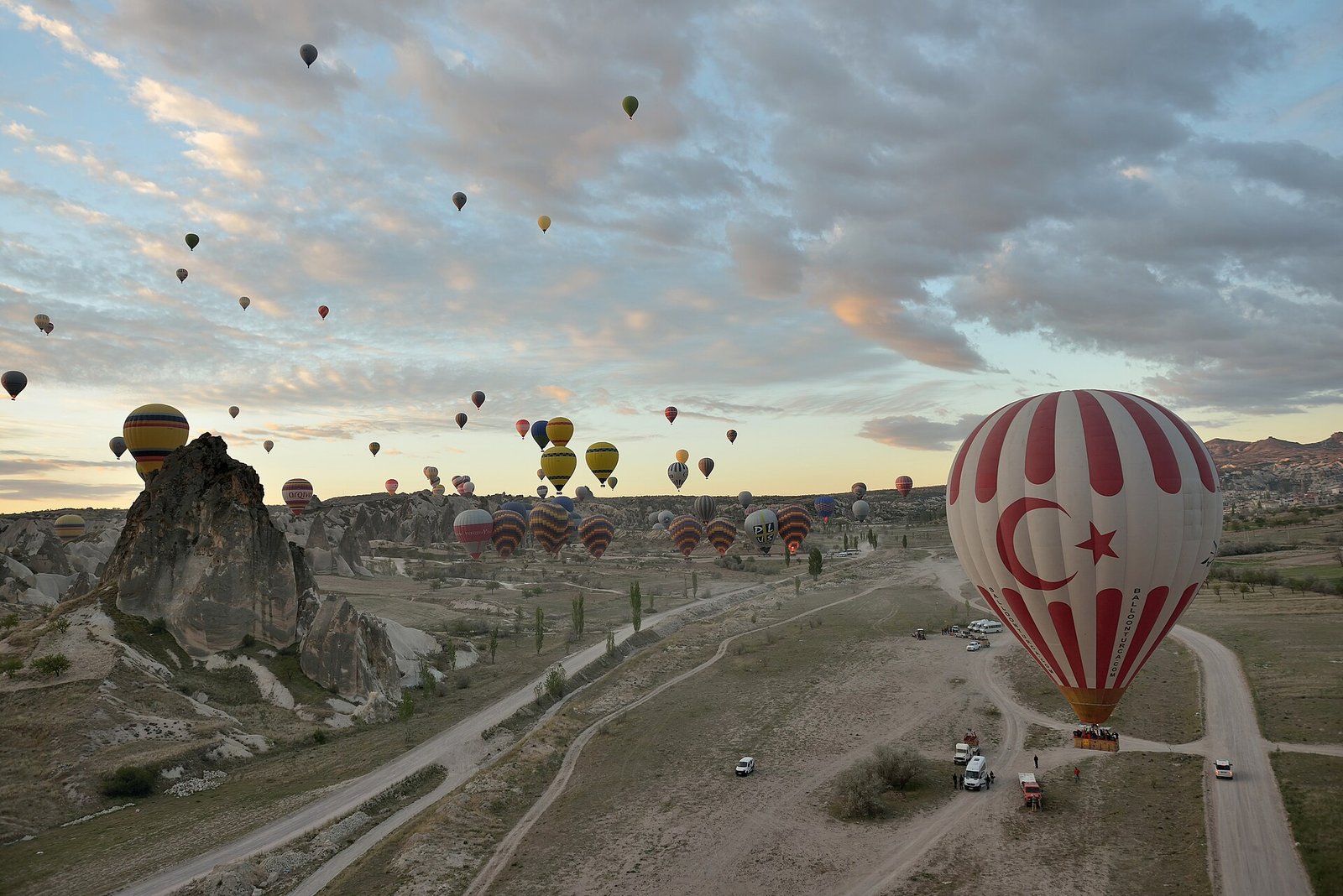Decenas de globos aerostaticos coloridos flotando al amanecer sobre las chimeneas de hadas y formaciones rocosas de Capadocia en Turquia, con un globo de la bandera turca