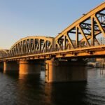 Puente de hierro sobre el rio Nilo en El Cairo bajo luz dorada del atardecer, con la estructura metalica iluminada y el horizonte urbano al fondo