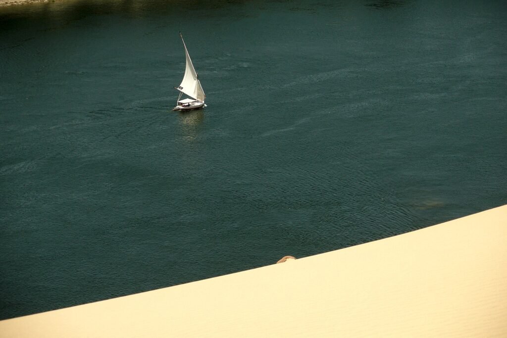 Felucca de vela blanca navegando por las aguas turquesa del rio Nilo junto a un banco de arena dorado en Egipto, escena ideal para preparar un viaje saludable