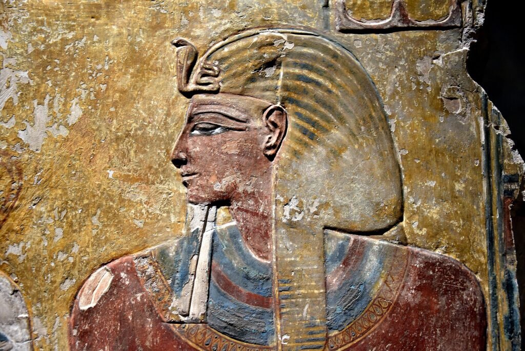 Relieve pintado de un faraón de perfil con tocado azul y dorado y piel rojiza sobre muro de ocre en una tumba del antiguo Egipto en Luxor