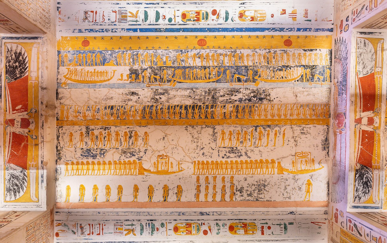 Techo de tumba faraonica en el Valle de los Reyes en Luxor Egipto con filas de figuras doradas y barcas solares pintadas sobre fondo crema y jeroglificos vivos