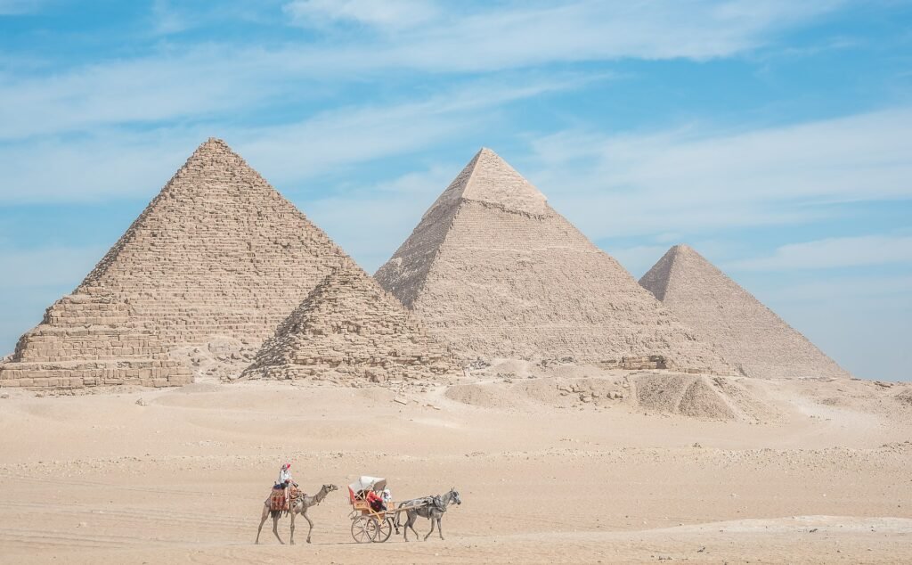 Camello y carruaje cruzando la arena ante las tres piramides de Giza bajo cielo azul