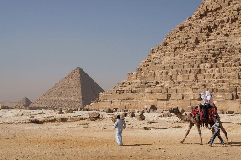 Familia viajando a Egipto con ninos montando en camello frente a las piramides de Giza