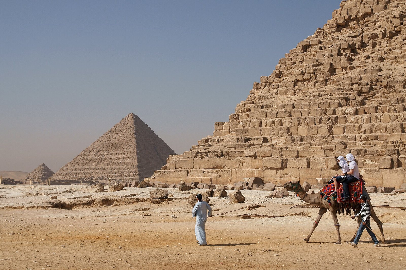 Familia viajando a Egipto con ninos montando en camello frente a las piramides de Giza