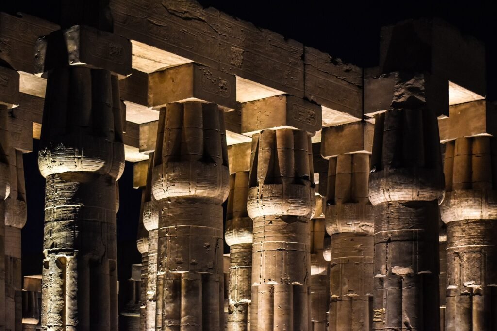 Columnas papiriformes del templo de Luxor iluminadas de noche con luz calida dorada contra el cielo negro, escena premium y limpia del patrimonio de Egipto