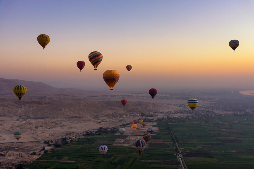 Decenas de globos aerostaticos coloridos sobrevolando el valle del Nilo y las colinas de Luxor al amanecer en Egipto, experiencia de lujo