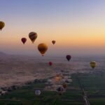 Decenas de globos aerostaticos coloridos sobrevolando el valle del Nilo y las colinas de Luxor al amanecer en Egipto, experiencia de lujo