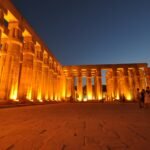Templo de Luxor iluminado de noche con columnas monumentales en tonos dorados y cielo azul oscuro, escena majestuosa de un viaje a Egipto