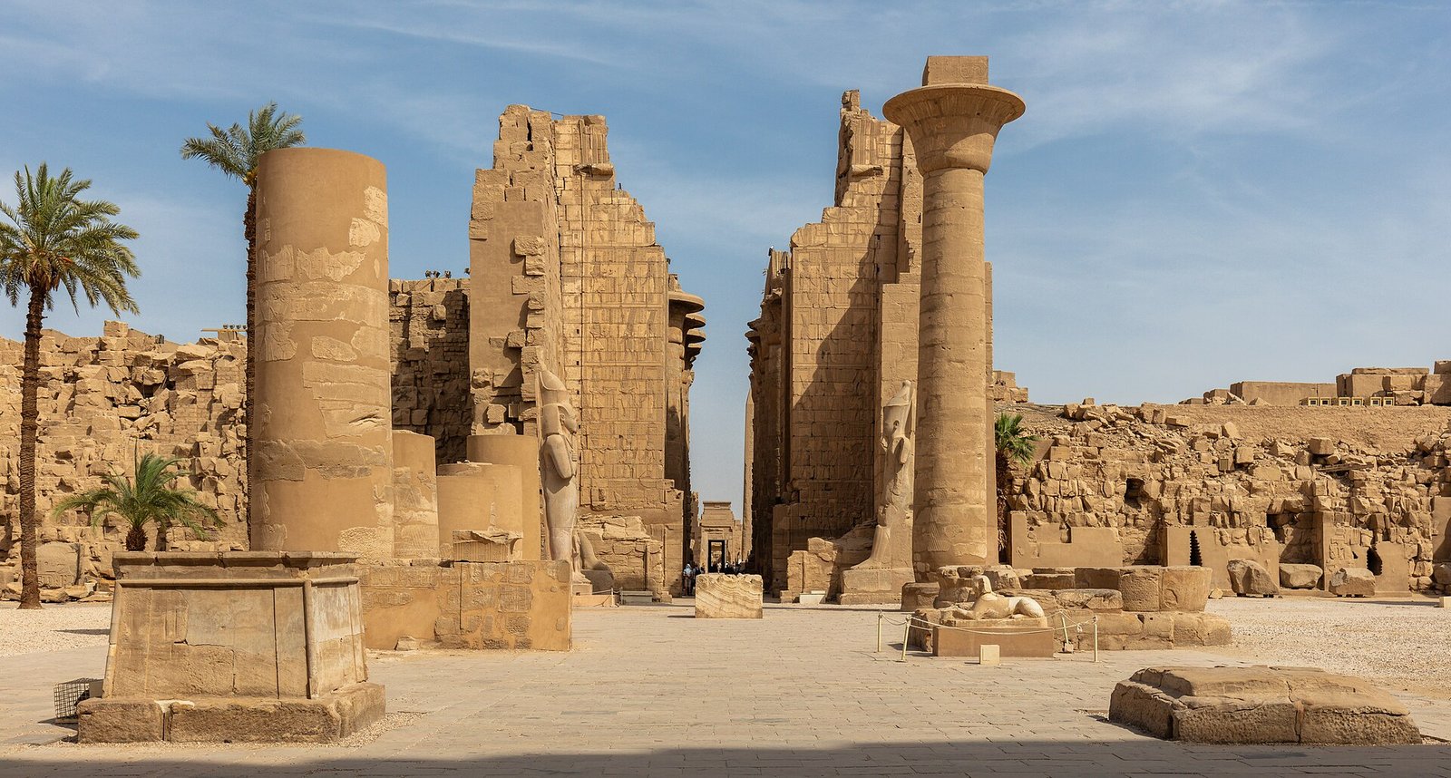 Templo de Karnak en Luxor a plena luz del dia con grandes columnas y muros antiguos, palmeras y cielo azul, vista panoramica monumental del antiguo Egipto