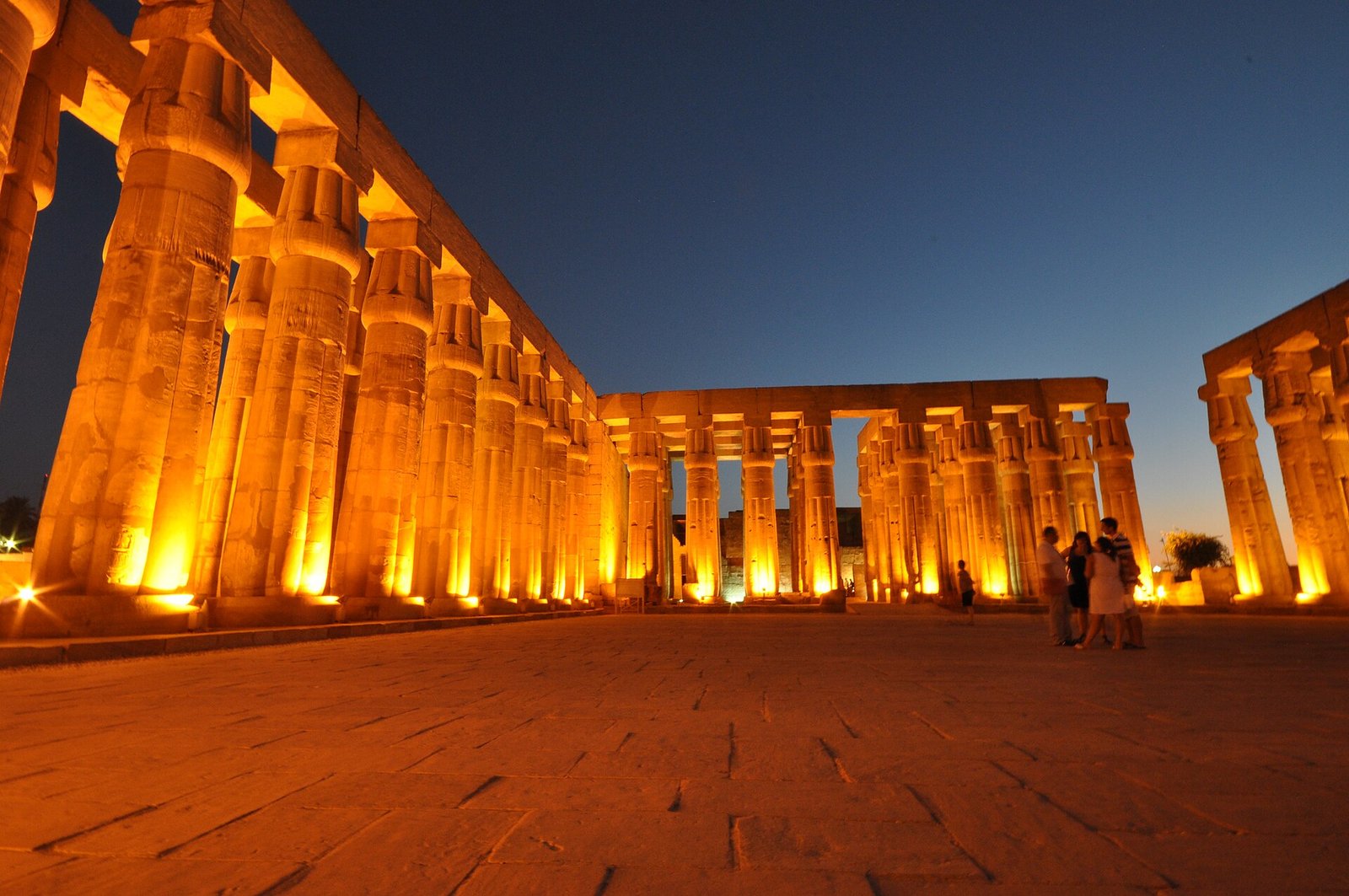 Templo de Luxor iluminado de noche con columnas monumentales en tonos dorados y cielo azul oscuro, escena majestuosa de un viaje a Egipto
