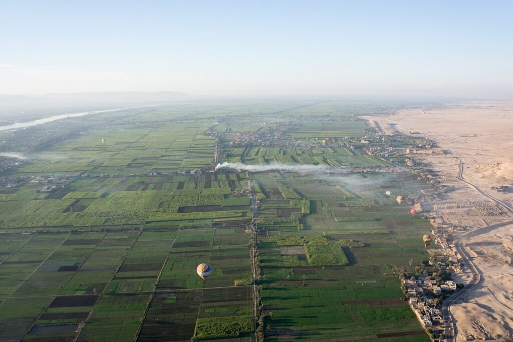 Vista aerea premium del valle del Nilo en Egipto con campos verdes geometricos, el rio brillando y el desierto al borde, con globo aerostatico al amanecer