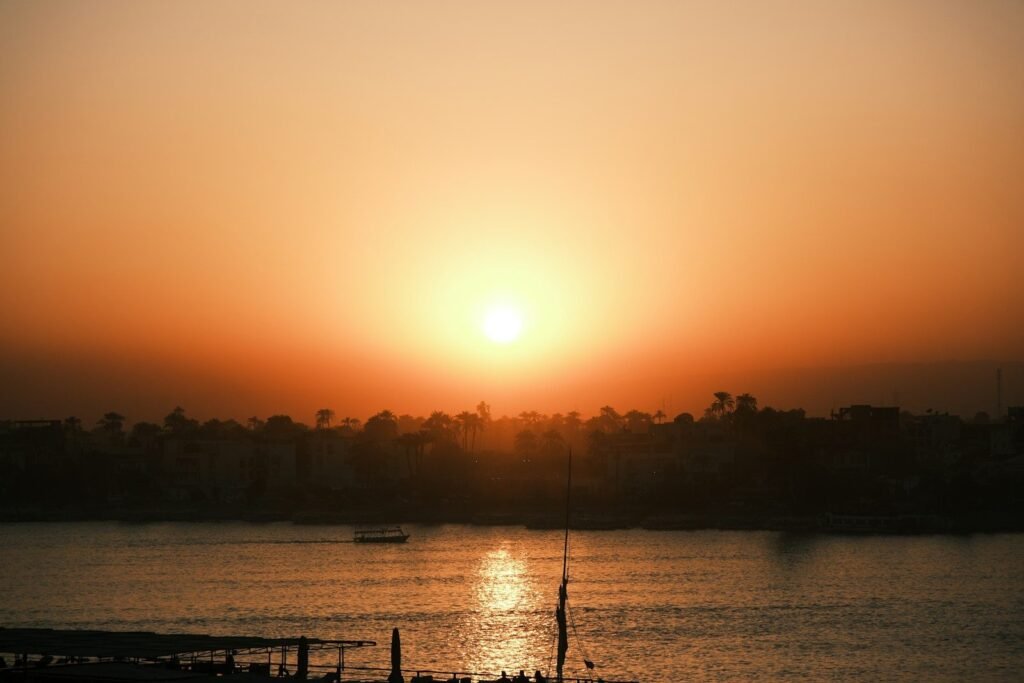 El sol se pone sobre el Nilo en Luxor, con palmeras en la orilla y el reflejo dorado en el agua