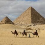 A camel train crossing the sand below the pyramid of Menkaure and the queens' pyramids at Giza