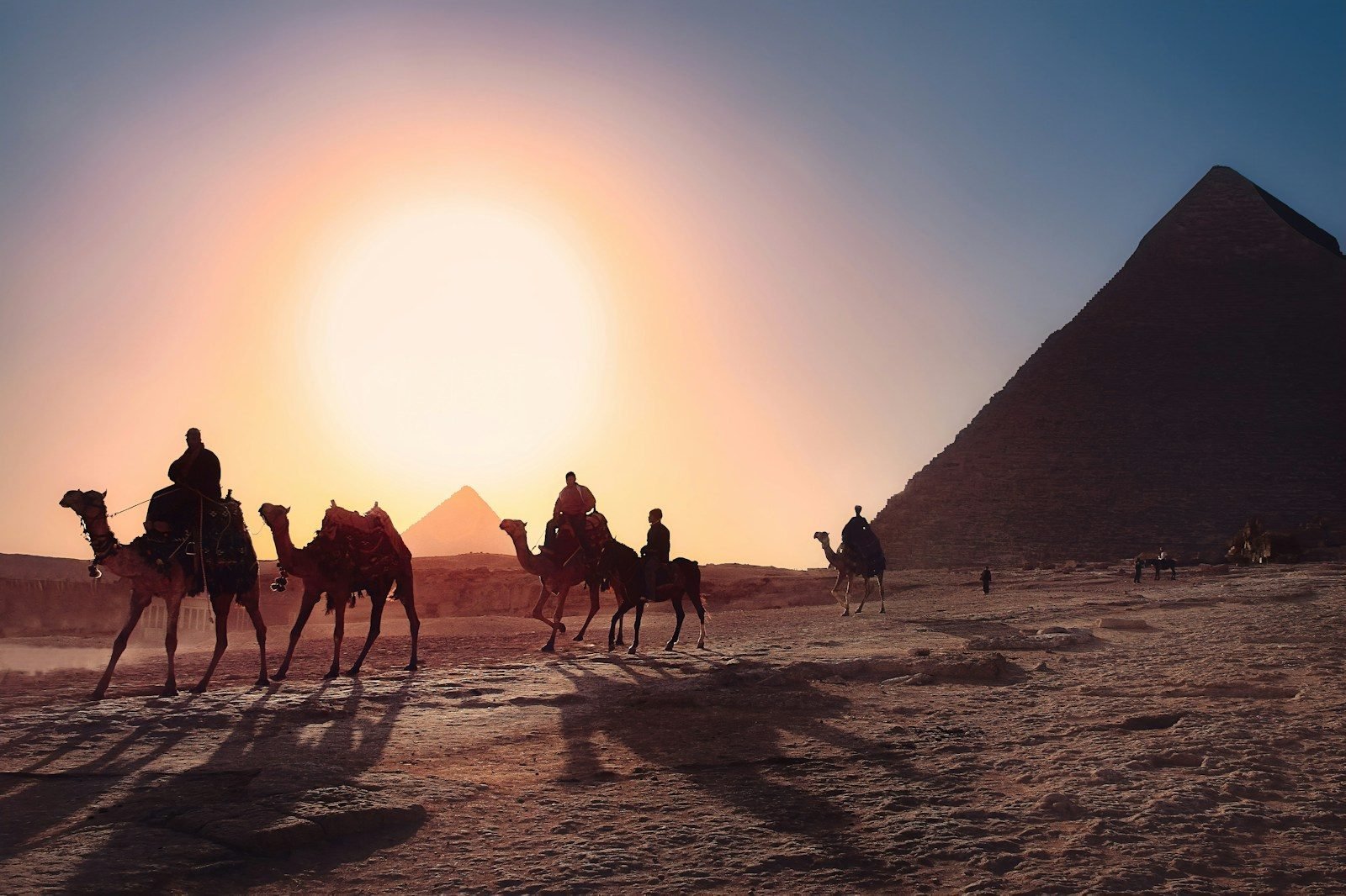 Una caravana de camellos cruzando la meseta de Giza al atardecer junto a la Gran Pirámide.