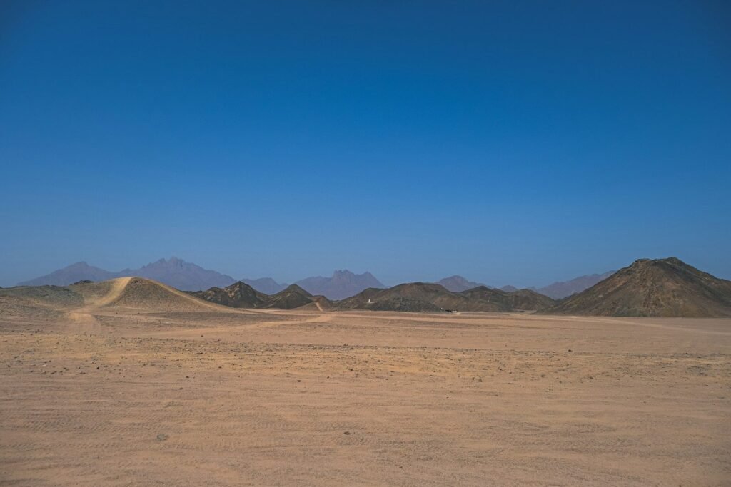 Una llanura del desierto egipcio con dunas y montañas bajo un cielo azul intenso