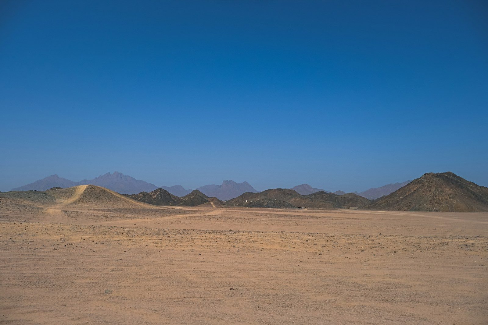Llanura del desierto egipcio con dunas y montañas bajo un cielo azul intenso.