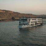 A cruise ship sailing the Nile near Aswan at dusk, desert cliffs along the bank
