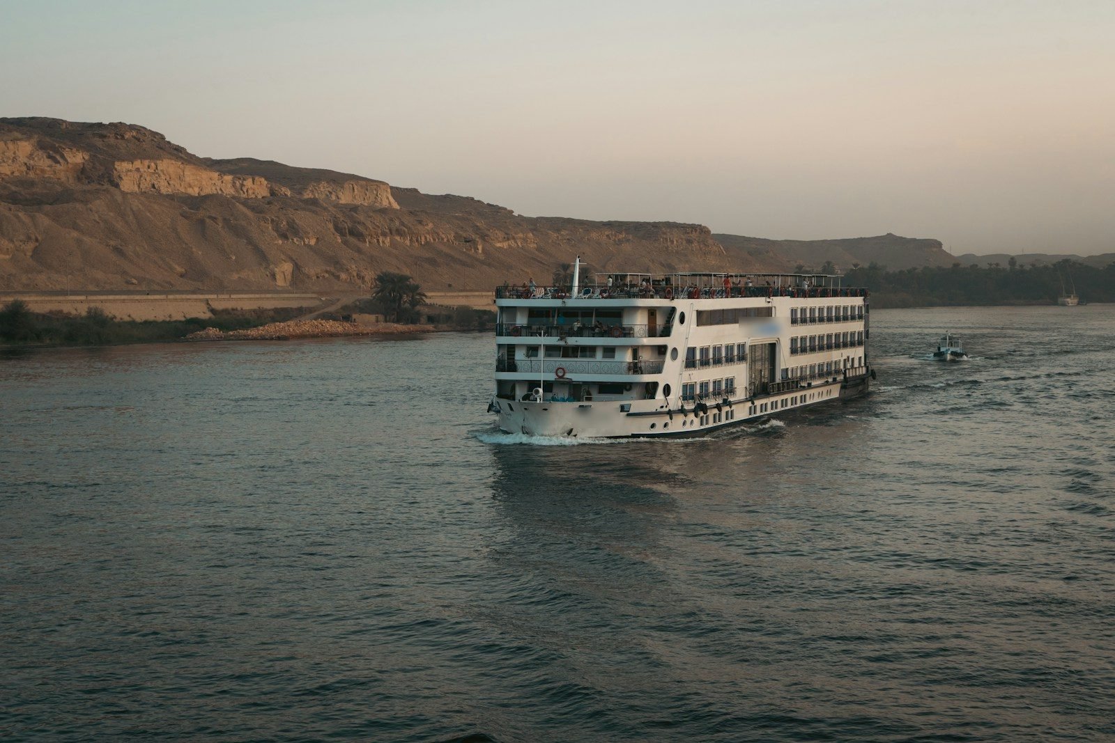 A cruise ship sailing the Nile near Aswan at dusk, desert cliffs along the bank