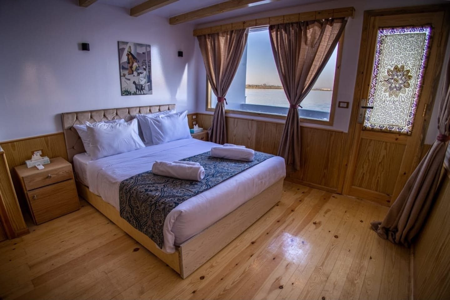 Cabina doble deluxe de la Akhenaton con cama doble, suelo de madera y ventana al río
