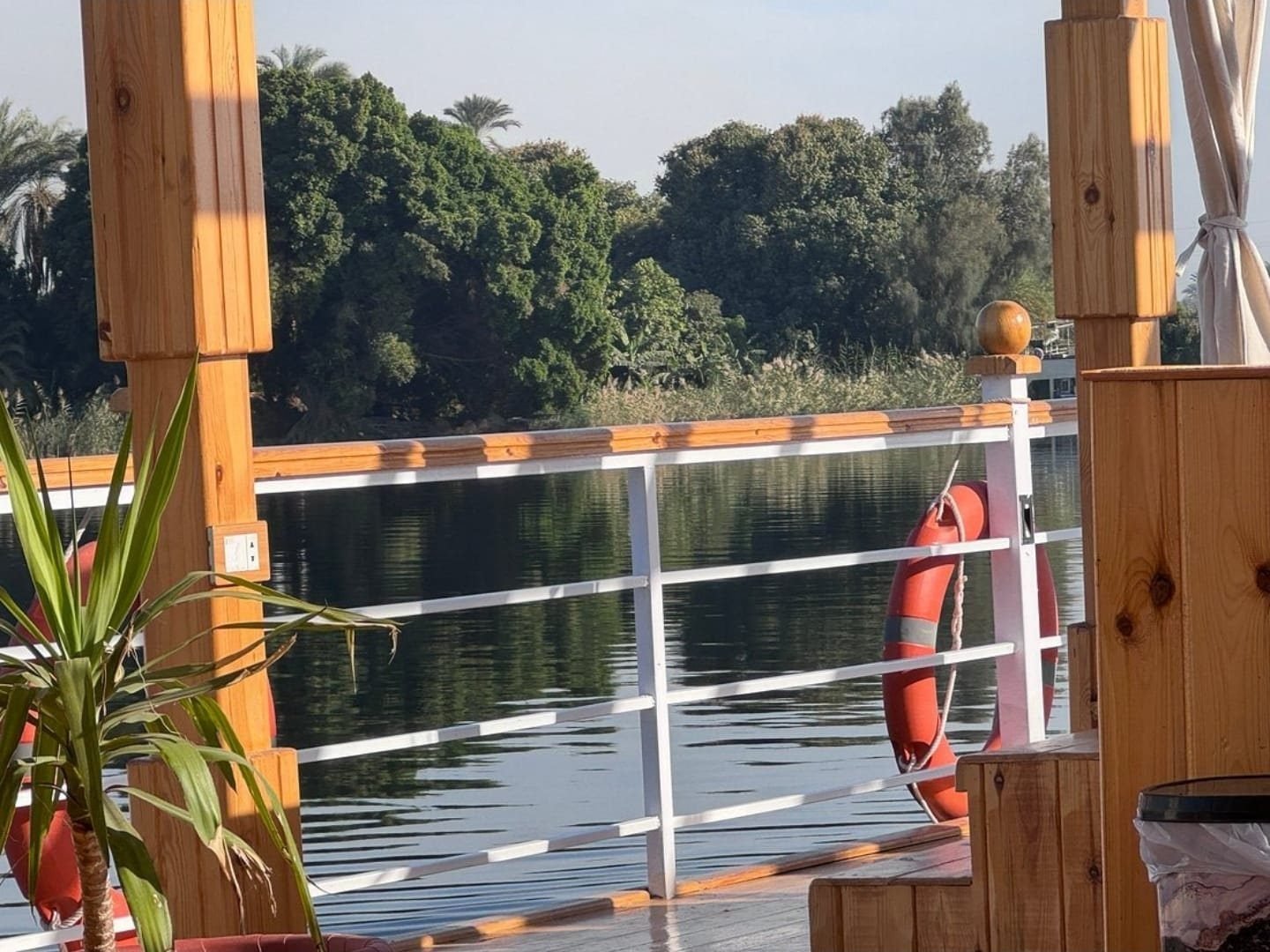 The green riverbank seen between the wooden posts of the Akhenaton deck