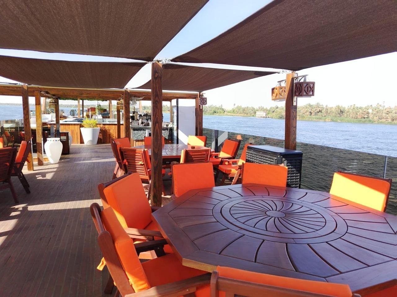 Wooden tables and orange chairs in the shade of the sails on the Iris deck