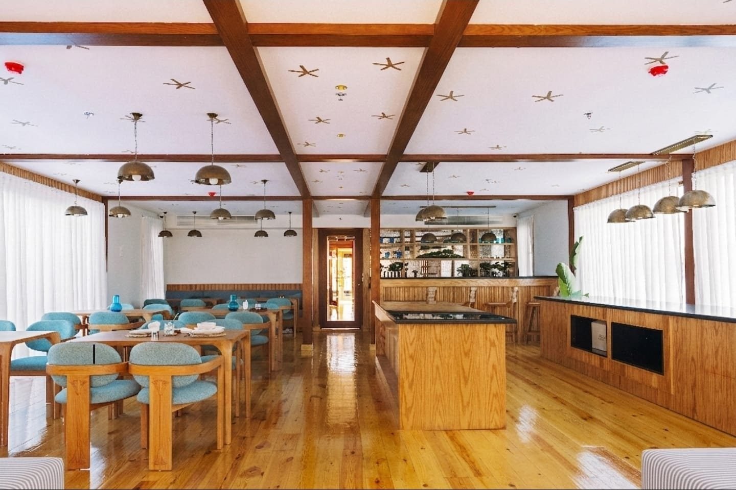 Restaurante de la Per-ba con mesas, sillas turquesa y barra de madera