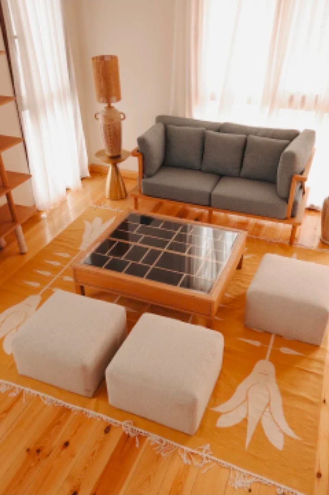Salón luminoso de la Per-ba con sofá, mesa baja y pufs sobre suelo de madera