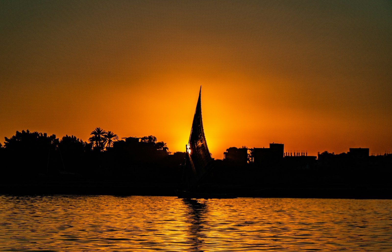 A felucca silhouetted against an orange sunset on the Nile at Luxor