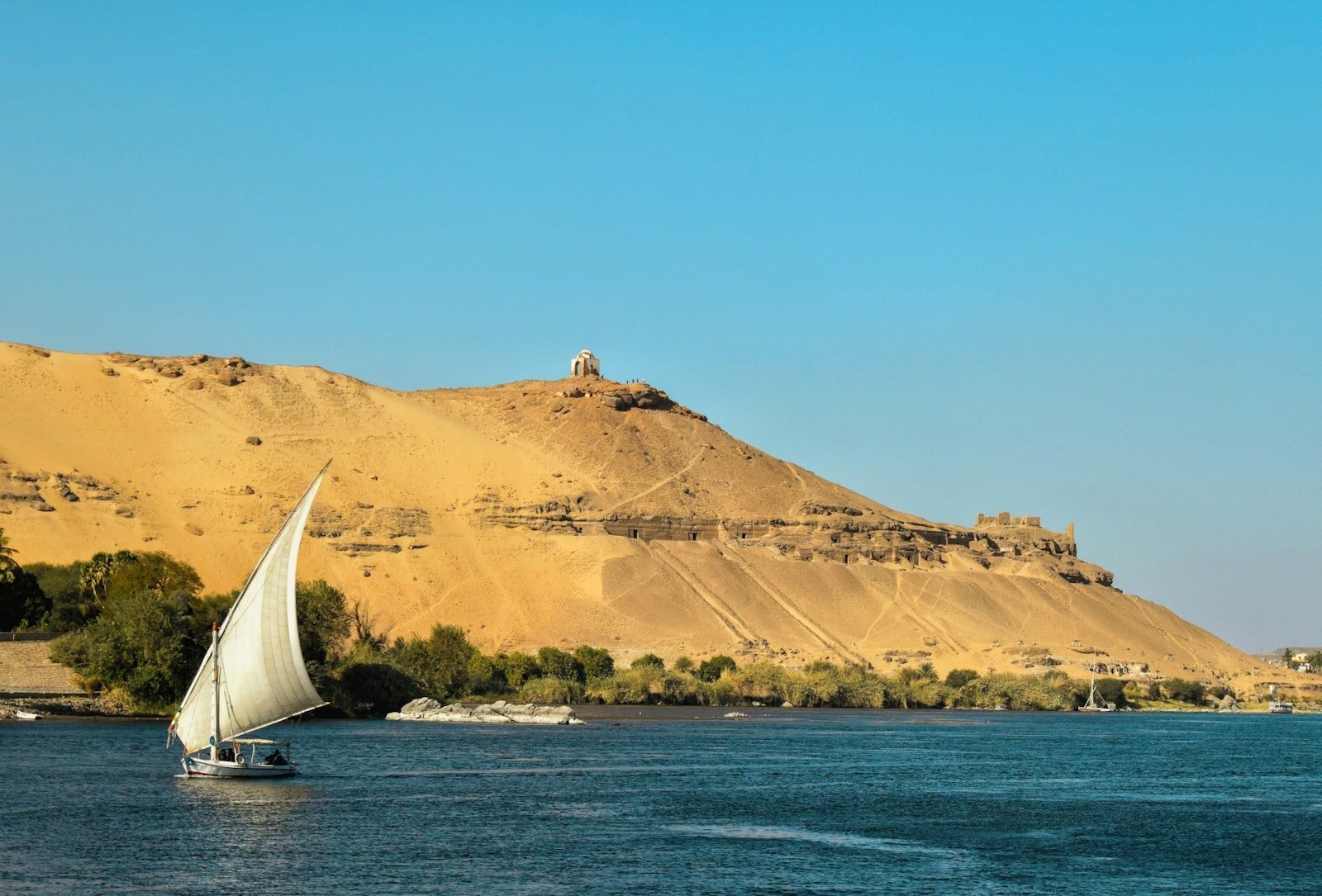 A felucca under sail on the Nile at Aswan, below the hill of Qubbet el-Hawa