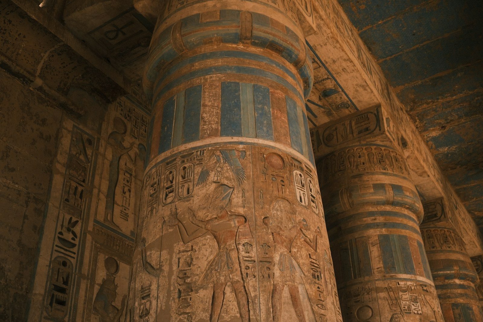 Columns of an Egyptian temple carved with hieroglyphs and reliefs that keep their blue and ochre paint