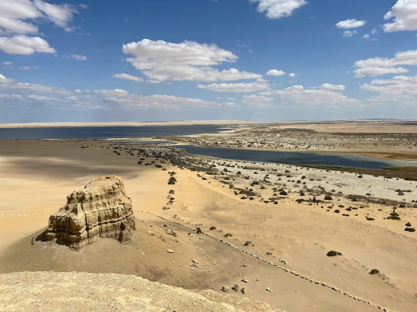 A desert lake in Fayoum seen from a dune, with wind-carved rocks and scrub on the sand