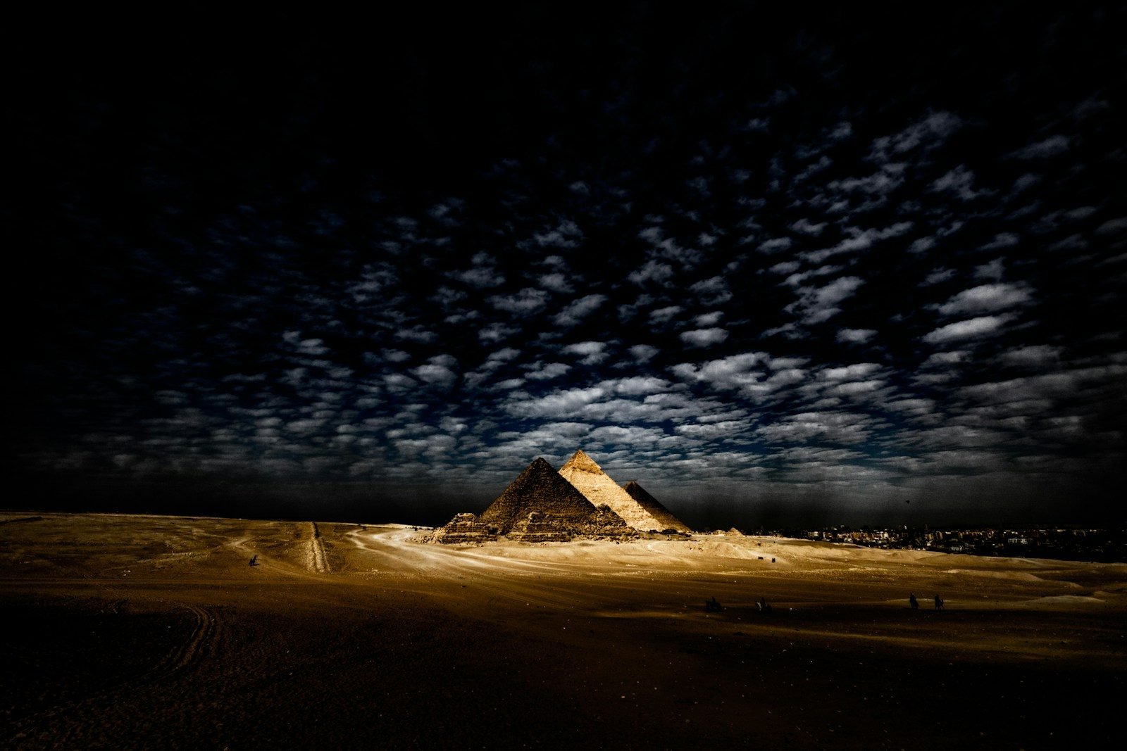 Las pirámides de Giza iluminadas de noche bajo un cielo con nubes alargadas