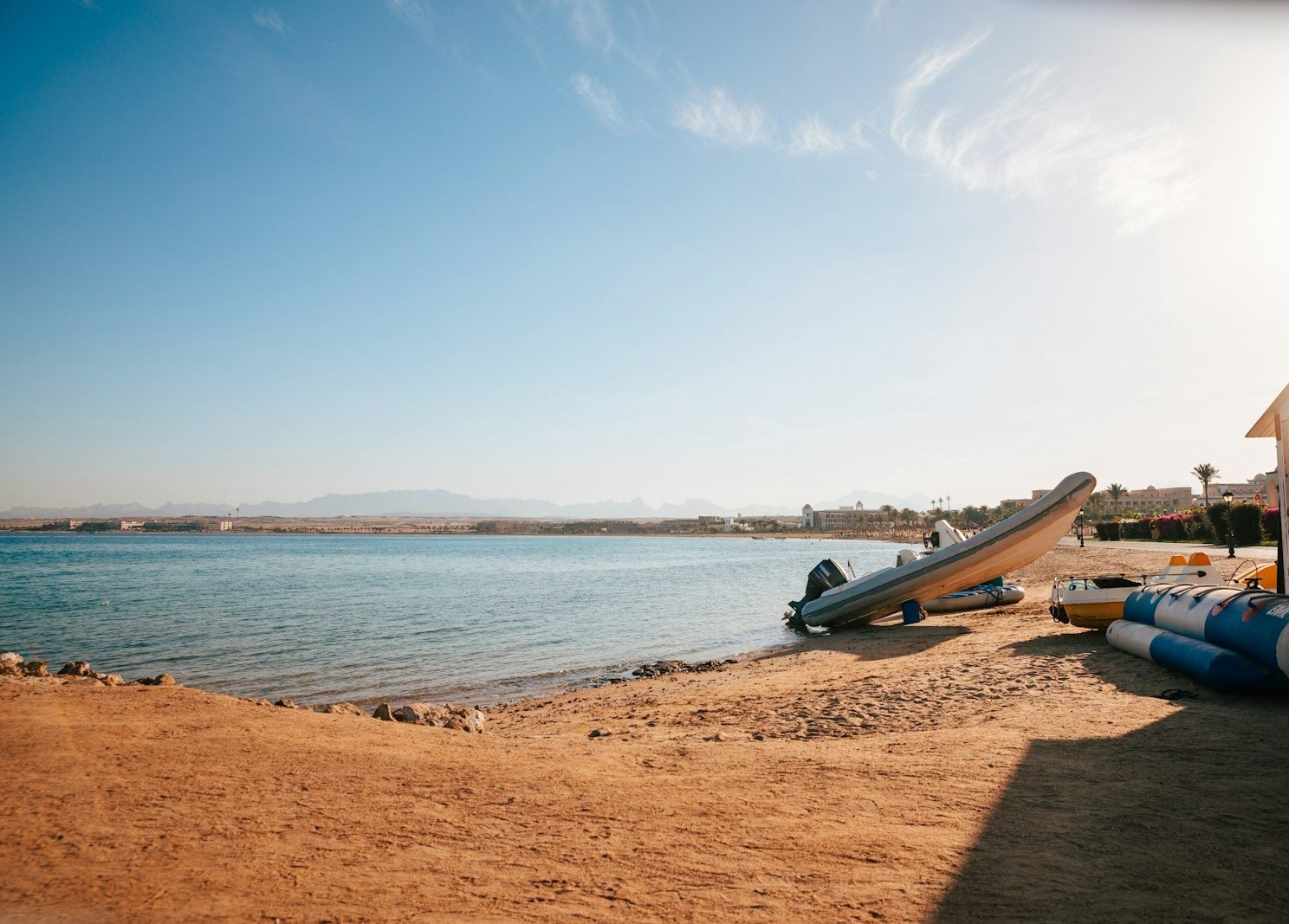 Playa de Sahl Hasheesh en el mar Rojo, con la bahía en calma, lanchas en la arena y las montañas al fondo