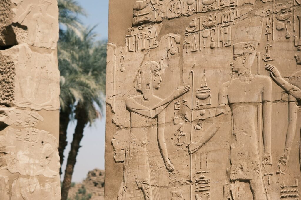Reliefs of a pharaoh before the gods on a wall of Karnak Temple, Luxor, with palms behind