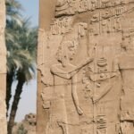 Reliefs of a pharaoh before the gods on a wall of Karnak Temple, Luxor, with palms behind