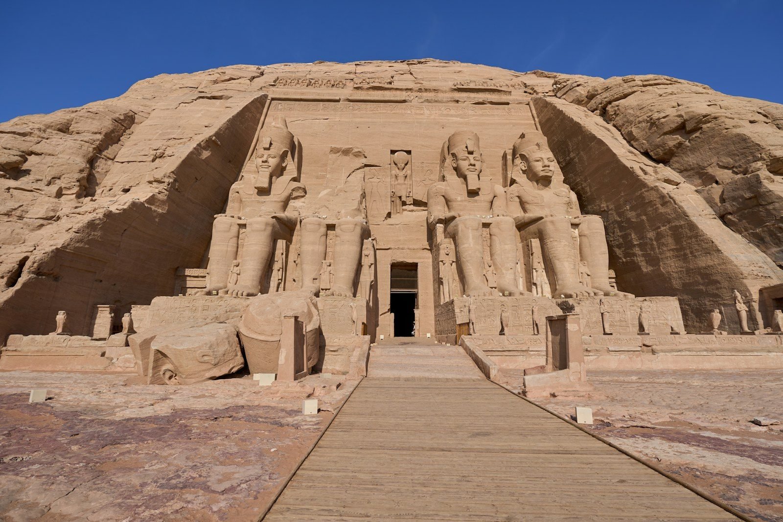 Fachada del Gran Templo de Abu Simbel con sus colosos sentados de Ramsés II, vista desde una pasarela de madera bajo un cielo azul.
