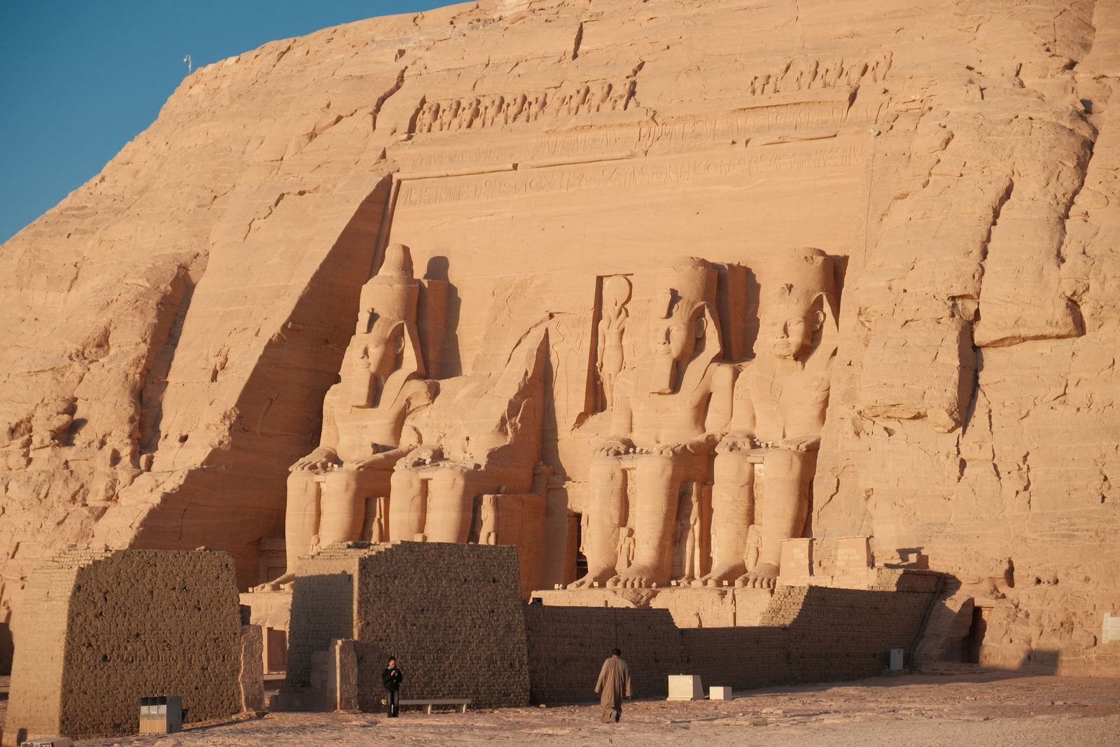 Colosos sentados tallados en la roca de la fachada del templo mayor de Abu Simbel, con luz cálida y dos pequeños visitantes junto a la base.