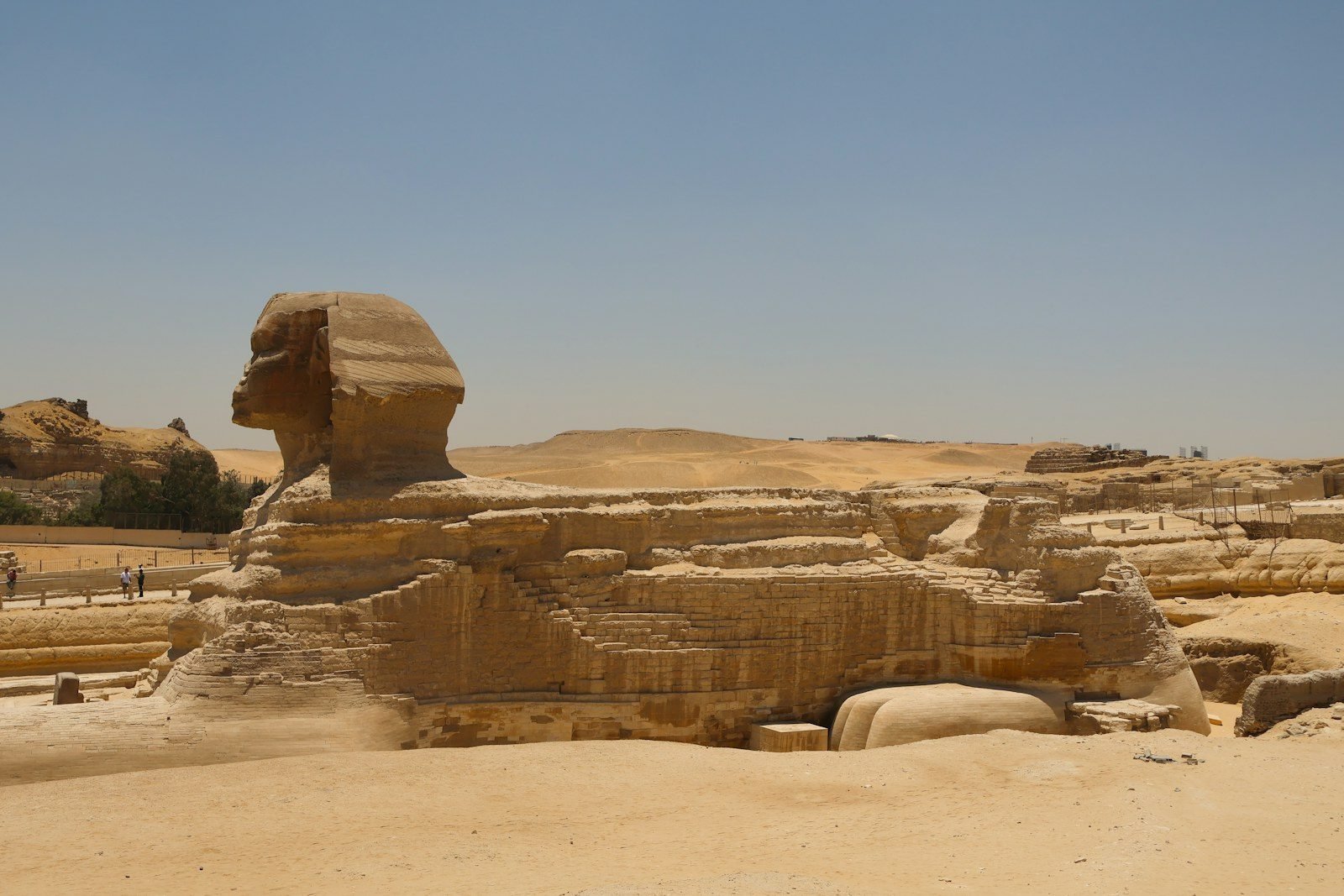 La Gran Esfinge de Giza de perfil, con todo el cuerpo, el flanco restaurado con sillares y el recinto que la rodea, bajo un cielo despejado.