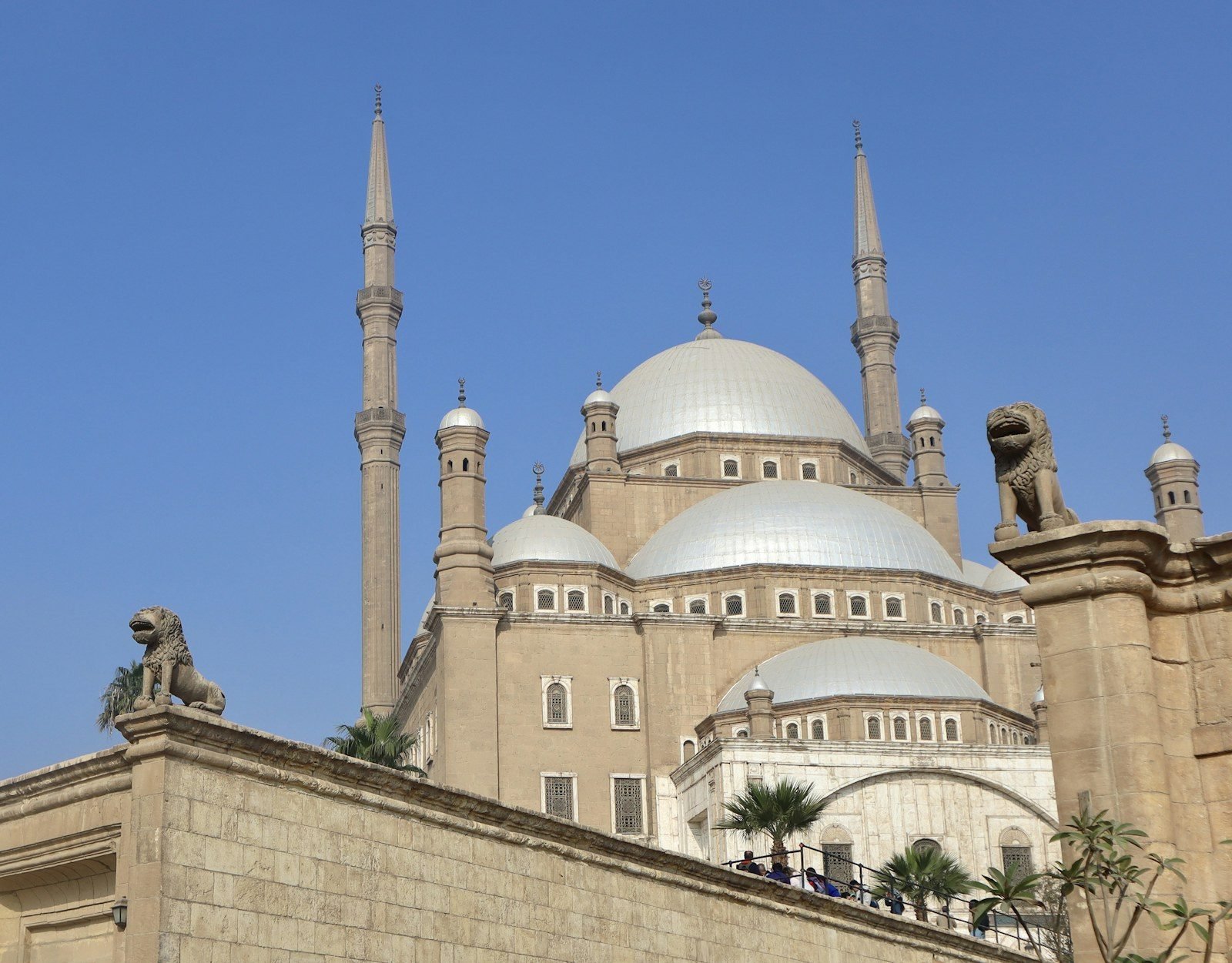 La mezquita de Mohamed Ali en la Ciudadela de El Cairo vista desde abajo, con sus dos minaretes esbeltos, sus cúpulas plateadas y dos leones de piedra sobre el muro.