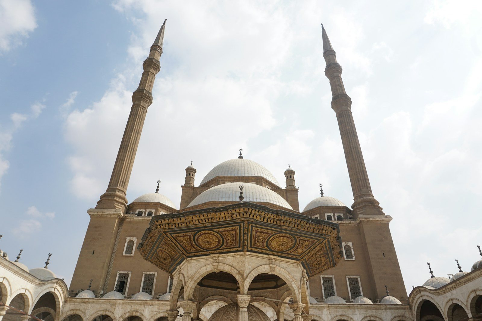 The Mosque of Muhammad Ali at the Cairo Citadel seen from its courtyard, with the gilded ablution fountain in the foreground, white domes and two slender minarets.