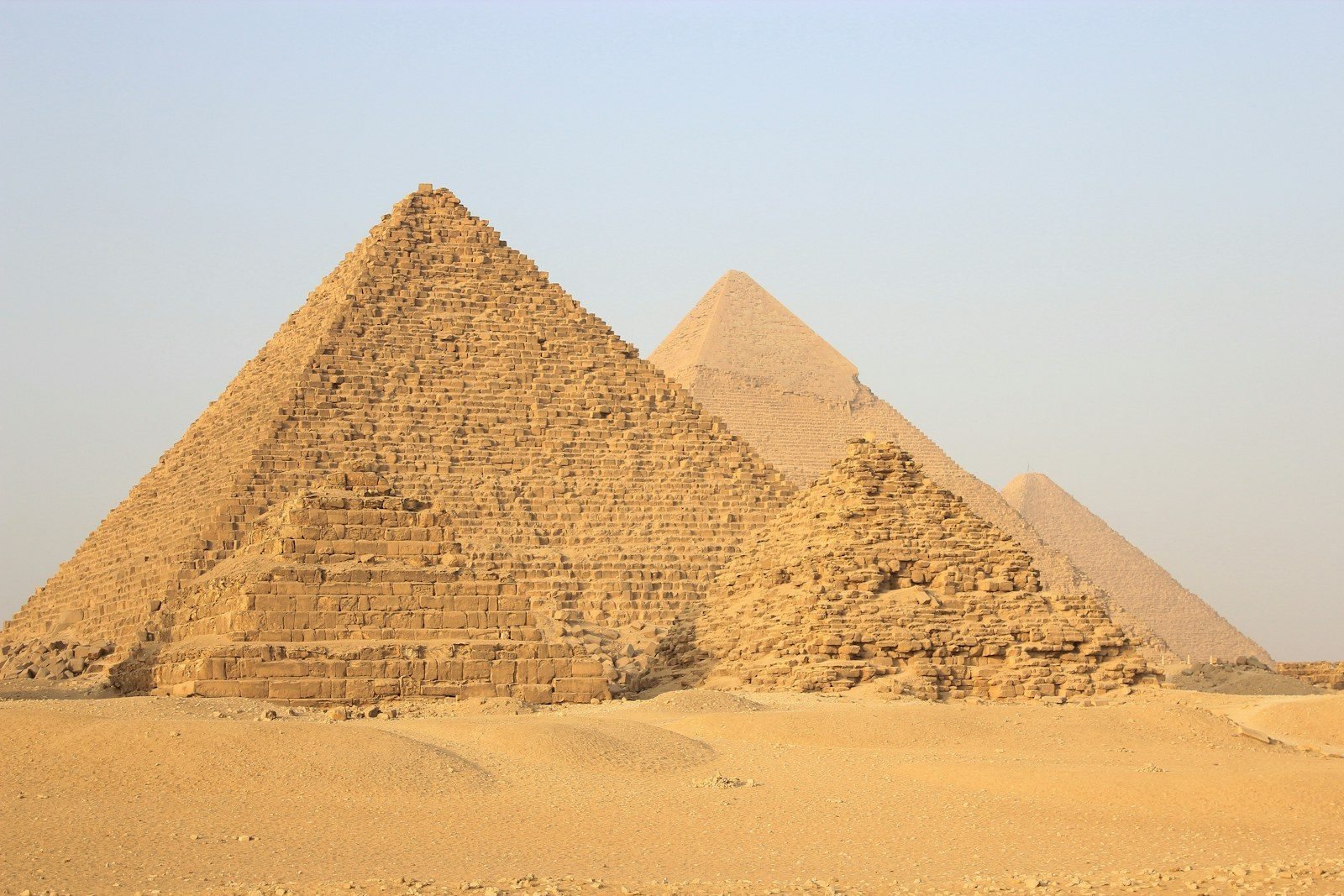 La pirámide de Micerinos en Giza con sus pequeñas pirámides satélite al pie, y las pirámides de Kefrén y Keops al fondo entre la bruma sobre la arena vacía.